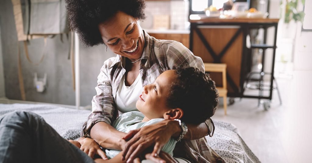 Happy african mother playing, having fun, hugging with her son at home; blog: Caring For Your Child’s Mental Wellness During a Pandemic